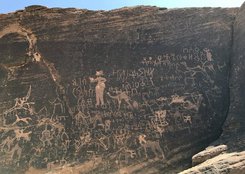 Rock carvings featuring various symbols, animals, and human figures, etched into a rugged stone surface.