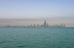 City skyline with numerous skyscrapers seen across a body of water under a clear sky.
