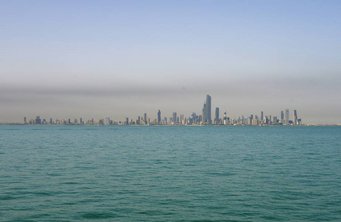 Haze over Kuwait. Source: MPIC City skyline with numerous skyscrapers seen across a body of water under a clear sky.