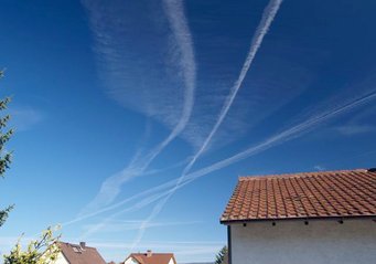The ice crystals of the contrails can persist for several hours at altitudes of about 8 to 12 kilometers in cold and humid conditions and form high clouds, so-called contrail cirrus. These clouds can have a warming or cooling effect locally, depending on the position of the sun and the background. Blue sky, contrails, roofs