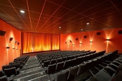 Cinema rows (gray seats) in an auditorium, curtain at the front (orange), walls on the right and left (orange), illuminated.