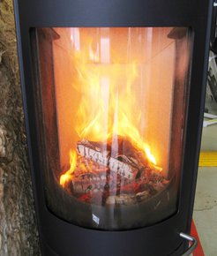 A black metal wood stove with a glass front displays burning logs, emitting bright orange flames and glowing embers.
