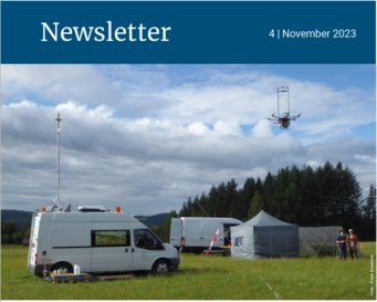 Field research site with vans, tents, and a drone in flight against a cloudy sky backdrop, surrounded by trees.