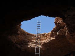 Eine Leiter führt aus einer Höhle hinaus.